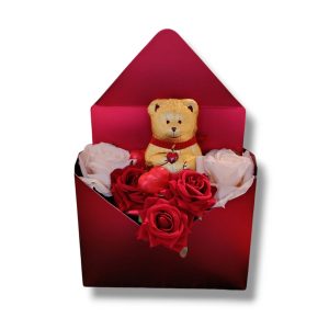 Confezione regalo rossa a forma di busta con orsacchiotto dorato, rose rosse e bianche, ideale per regali romantici.